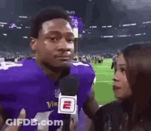 A Man In A Purple Vikings Jersey Is Being Interviewed By A Woman In Front Of A Microphone . GIF