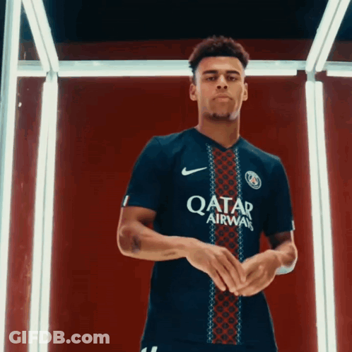 A Man In A Qatar Airways Jersey Stands In Front Of A Red Background GIF