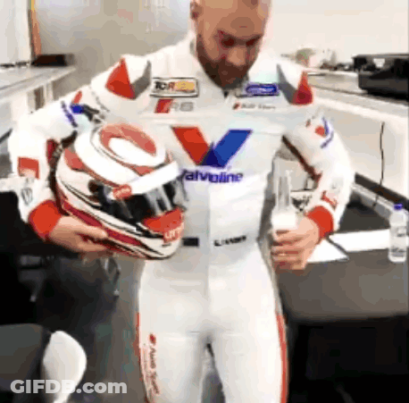A Man In A Racing Suit Is Holding A Helmet And Drinking A Glass Of Wine . GIF