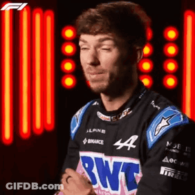 A Man In A Racing Suit Is Standing In Front Of A Neon Light . GIF