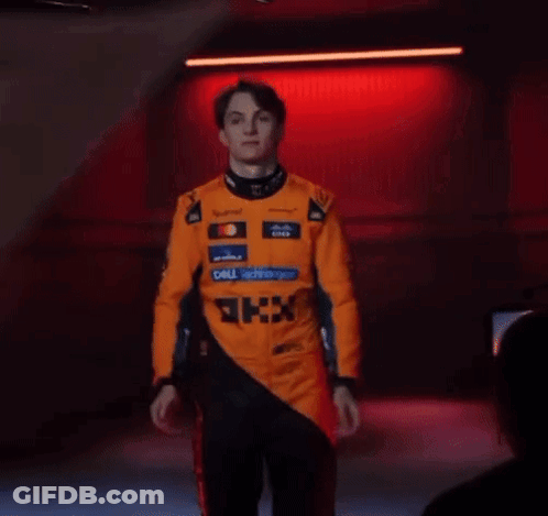 A Man In A Racing Suit Is Standing In Front Of A Red Light . GIF