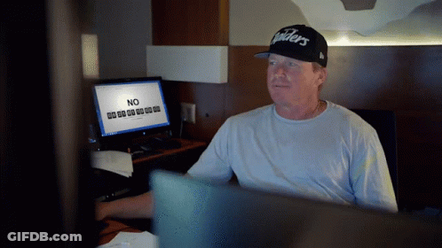 A Man In A Raiders Hat Sits In Front Of A Computer GIF