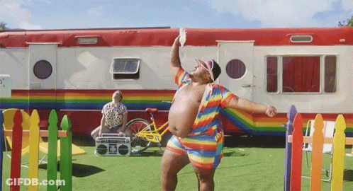A Man In A Rainbow Outfit Stands In Front Of A Rainbow Trailer GIF