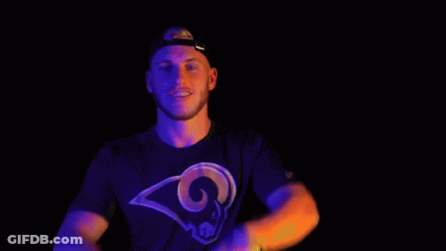 A Man In A Rams T-Shirt Is Making A Peace Sign With His Hands In Front Of His Face . GIF