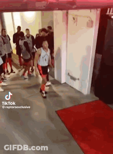 A Man In A Raptors Jersey Is Walking Through A Hallway Surrounded By People . GIF