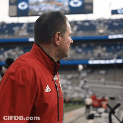 A Man In A Red Adidas Jacket Stands In Front Of A Crowd GIF