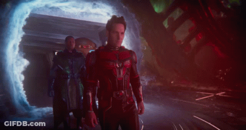 A Man In A Red And Black Costume Stands In Front Of A Portal GIF