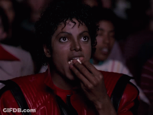 A Man In A Red And Black Jacket Is Eating Popcorn GIF