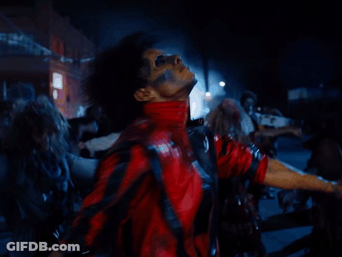 A Man In A Red And Black Jacket Is Surrounded By A Crowd Of Zombies GIF