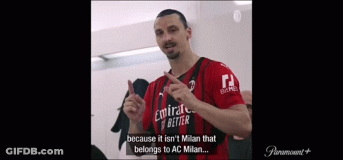 A Man In A Red And Black Jersey Is Standing In A Locker Room And Talking . GIF