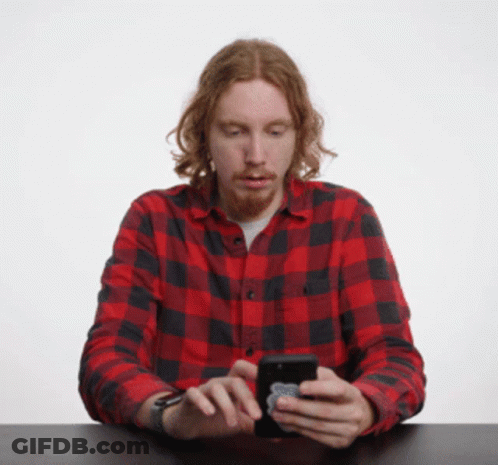A Man In A Red And Black Plaid Shirt Is Looking At His Cell Phone GIF