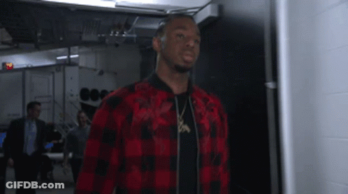 A Man In A Red And Black Plaid Shirt Is Standing In A Hallway GIF