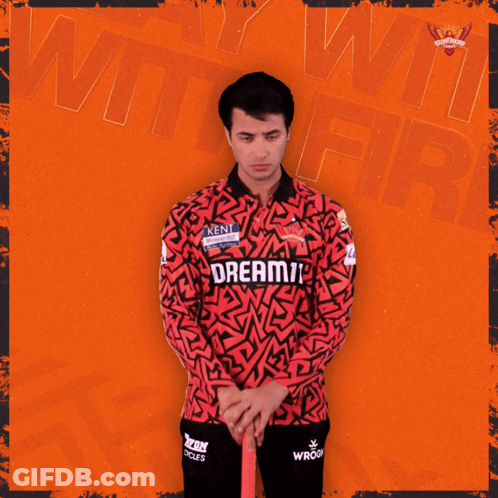A Man In A Red And Black Shirt Holds A Ton Cricket Bat GIF