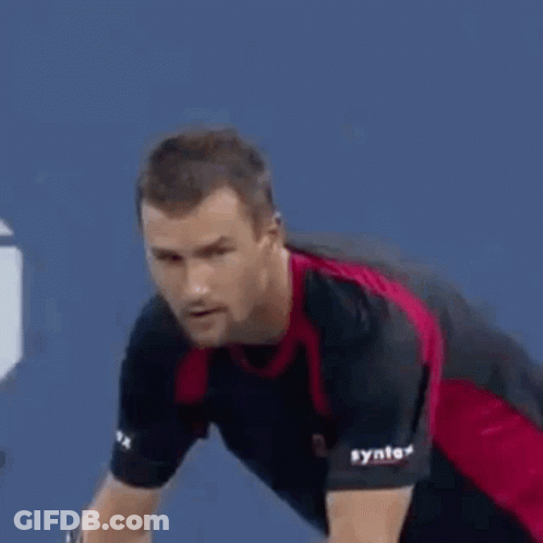 A Man In A Red And Black Shirt Is Playing Tennis On A Court . GIF