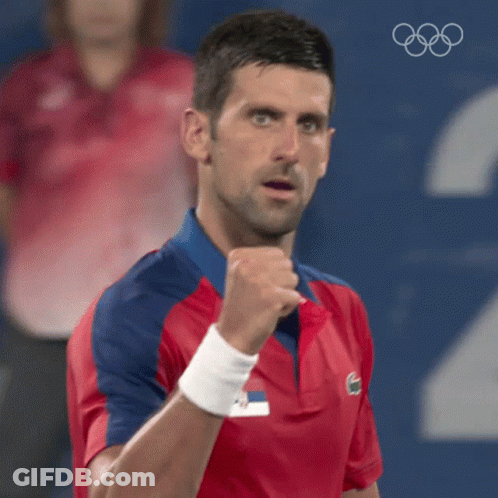 A Man In A Red And Blue Shirt Is Holding His Fist In The Air While Wearing A Wristband . GIF