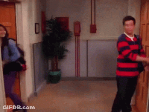 A Man In A Red And Blue Striped Shirt Is Opening A Door While A Woman Looks On . GIF