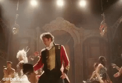 A Man In A Red And Gold Uniform Is Dancing On A Stage With A Group Of People . GIF
