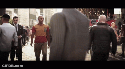 A Man In A Red And Orange Shirt Walks Down A Street With Other People GIF