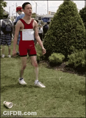 A Man In A Red And White Leotard Is Walking In The Grass GIF