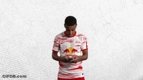 A Man In A Red And White Red Bull Shirt Holds A Cell Phone GIF