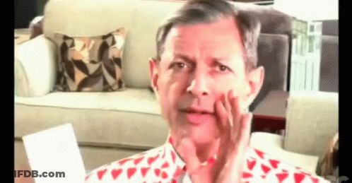A Man In A Red And White Shirt Is Sitting In Front Of A Couch Making A Funny Face . GIF