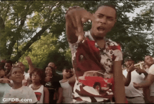 A Man In A Red And White Shirt Is Standing In Front Of A Crowd GIF