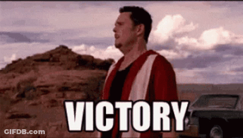 A Man In A Red And White Shirt Is Standing In The Desert With The Word Victory Written On The Ground . GIF