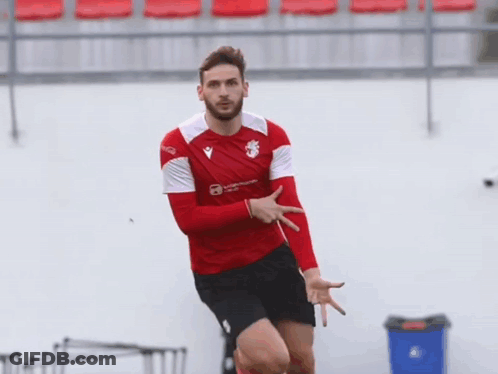 A Man In A Red And White Shirt With A Lion On It Is Pointing At Something GIF