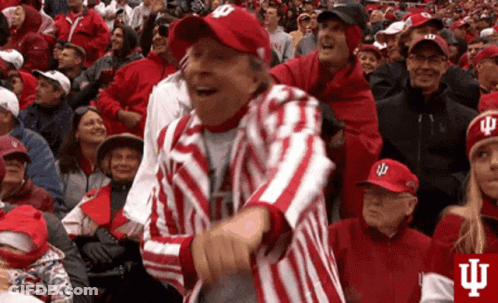 A Man In A Red And White Striped Jacket And Hat Is Dancing In A Crowd Of People . GIF