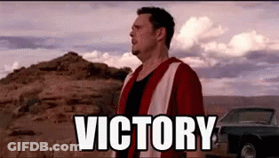 A Man In A Red And White Vest Is Standing In The Desert With The Words `` Victory '' Above Him . GIF