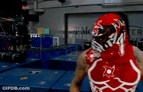 A Man In A Red And White Wrestling Outfit Stands In Front Of A T Mobile Sign GIF