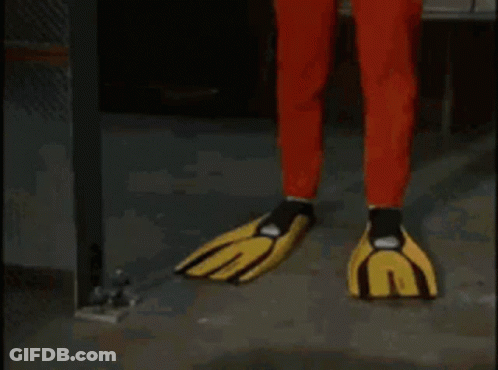 A Man In A Red And Yellow Jumpsuit And Yellow Gloves Is Standing In A Hallway . GIF