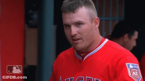 A Man In A Red Angels Jersey Is Standing In The Dugout . GIF