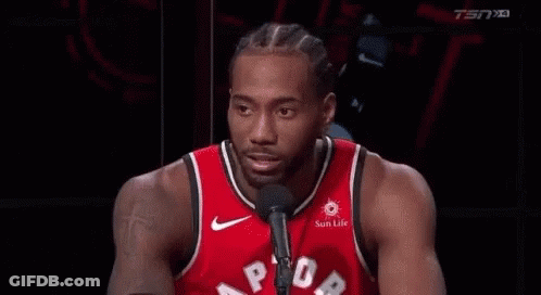 A Man In A Red Basketball Jersey Is Talking Into A Microphone . GIF