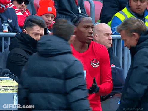 A Man In A Red Canada Shirt Stands In A Crowd Of People GIF