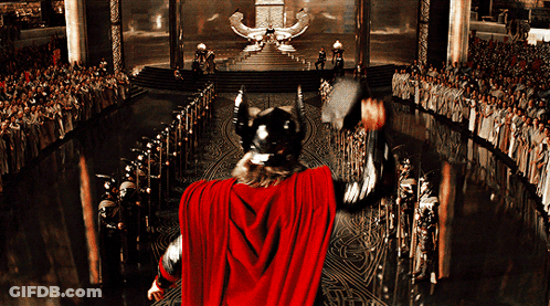 A Man In A Red Cape Is Holding A Hammer In Front Of A Large Crowd GIF