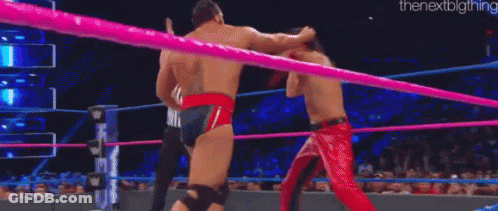 A Man In A Red Cape Is Wrestling Another Man In A Ring . GIF
