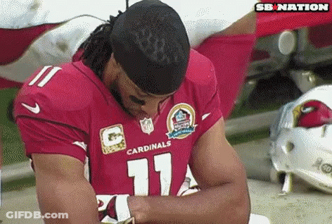 A Man In A Red Cardinals Jersey Is Sitting On The Ground With His Head Down . GIF