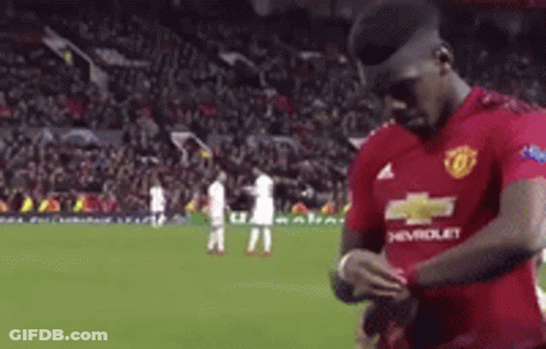 A Man In A Red Chevrolet Jersey Is Standing On A Soccer Field Looking At His Watch . GIF