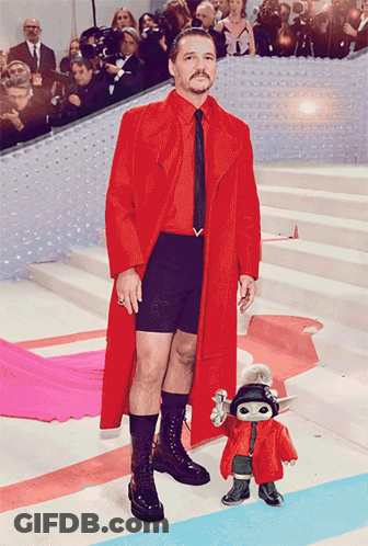 A Man In A Red Coat And Black Shorts Stands Next To A Toy GIF