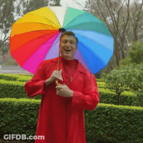A Man In A Red Coat Holding A Colorful Umbrella GIF