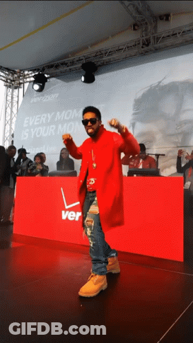 A Man In A Red Coat Is Dancing In Front Of A Sign That Says Verizon GIF