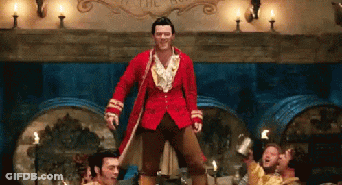 A Man In A Red Coat Is Standing On One Leg In Front Of A Group Of Men In A Room . GIF