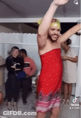 A Man In A Red Dress Is Dancing In Front Of A Group Of People .. GIF
