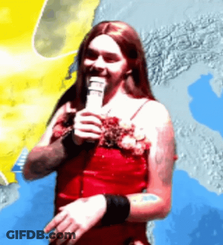 A Man In A Red Dress Is Holding A Microphone In His Hand GIF