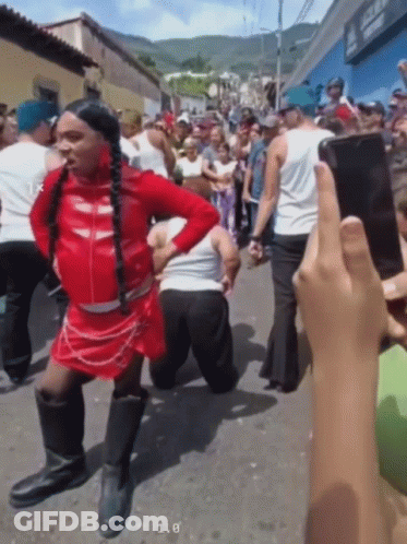 A Man In A Red Dress Is Kneeling Down In Front Of A Crowd While Someone Takes A Picture Of Him GIF