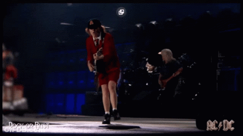 A Man In A Red Dress Is Playing A Guitar On A Stage With Ac/dc Written On The Bottom GIF