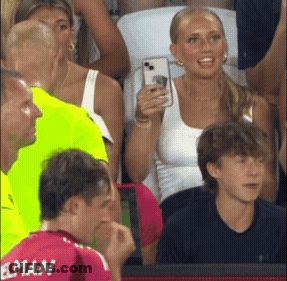 A Man In A Red Elman Jersey Looks At A Woman Taking A Picture GIF