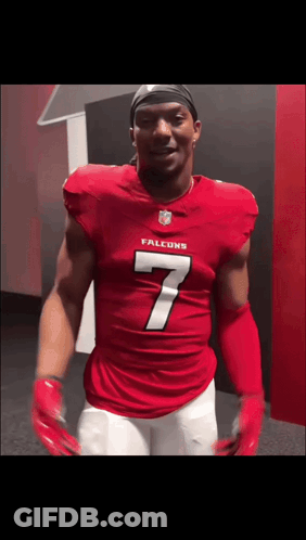 A Man In A Red Falcons Jersey Is Standing In A Locker Room GIF