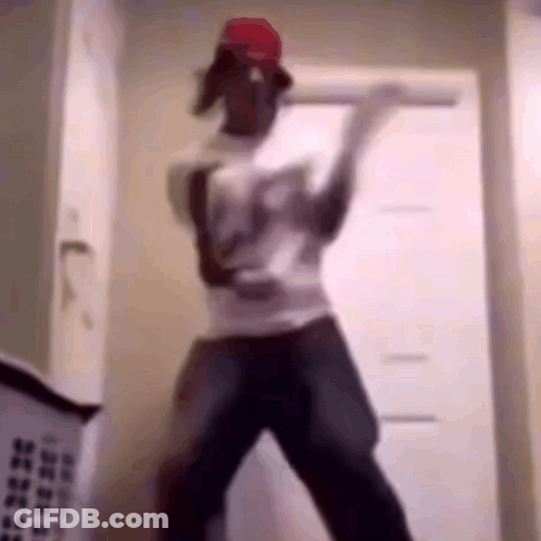 A Man In A Red Hat Is Dancing In A Room With A Laundry Basket Behind Him . GIF
